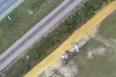 Aerial view of road, railroad tracks, clay road, and group managing drone flight
